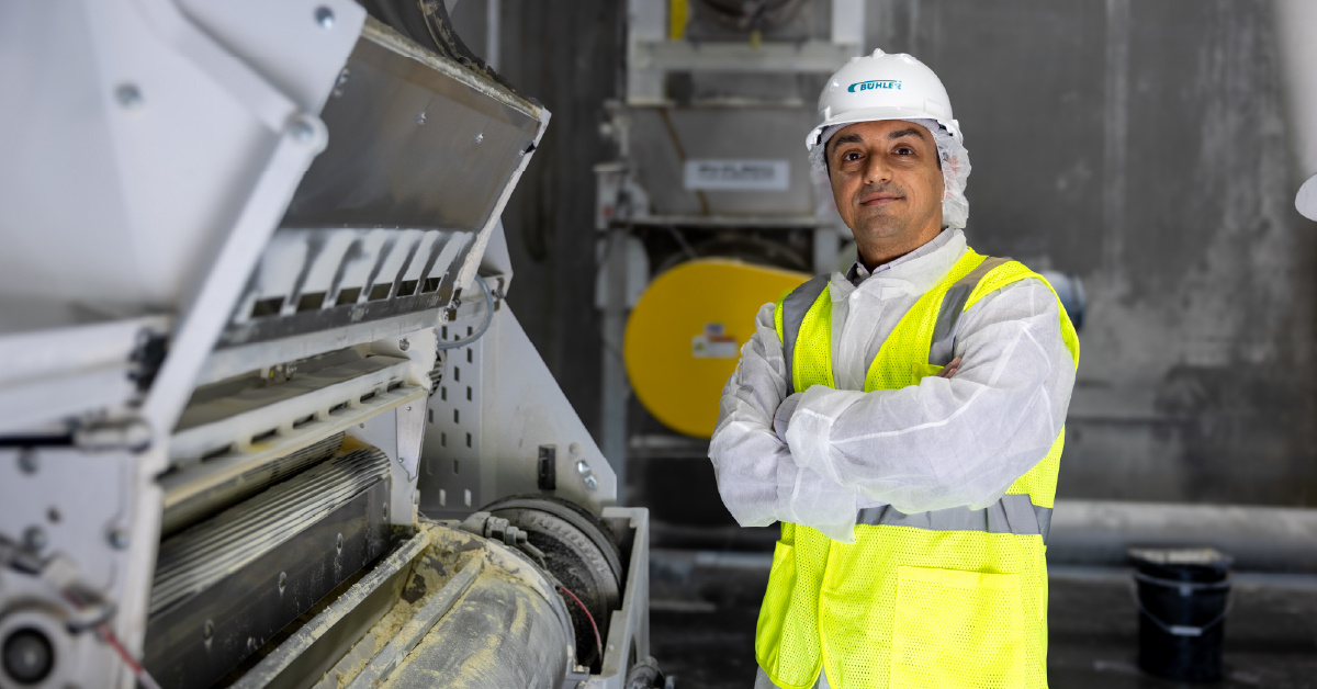 PURIS Dawson pea processing plant worker wearing yellow protective vest and white helmet stands by processing equipment.